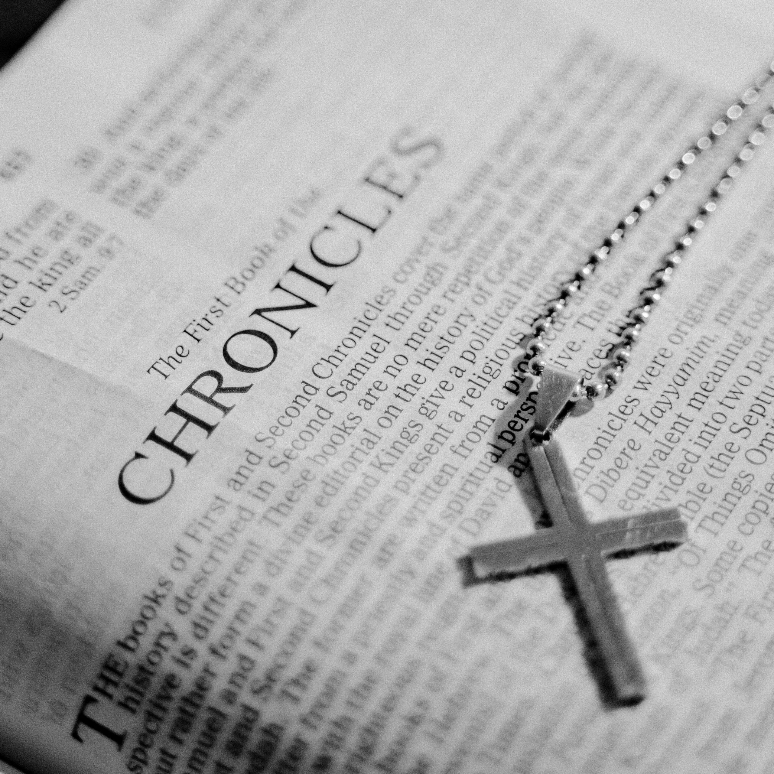 Black and white photo of a Bible page with a cross pendant on top, symbolizing faith.